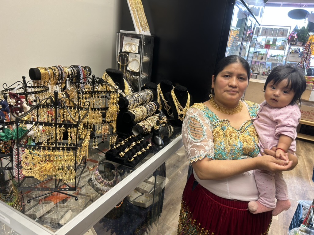 Maria holding her daughter beside the jewelry display at Guallpa Latin Market